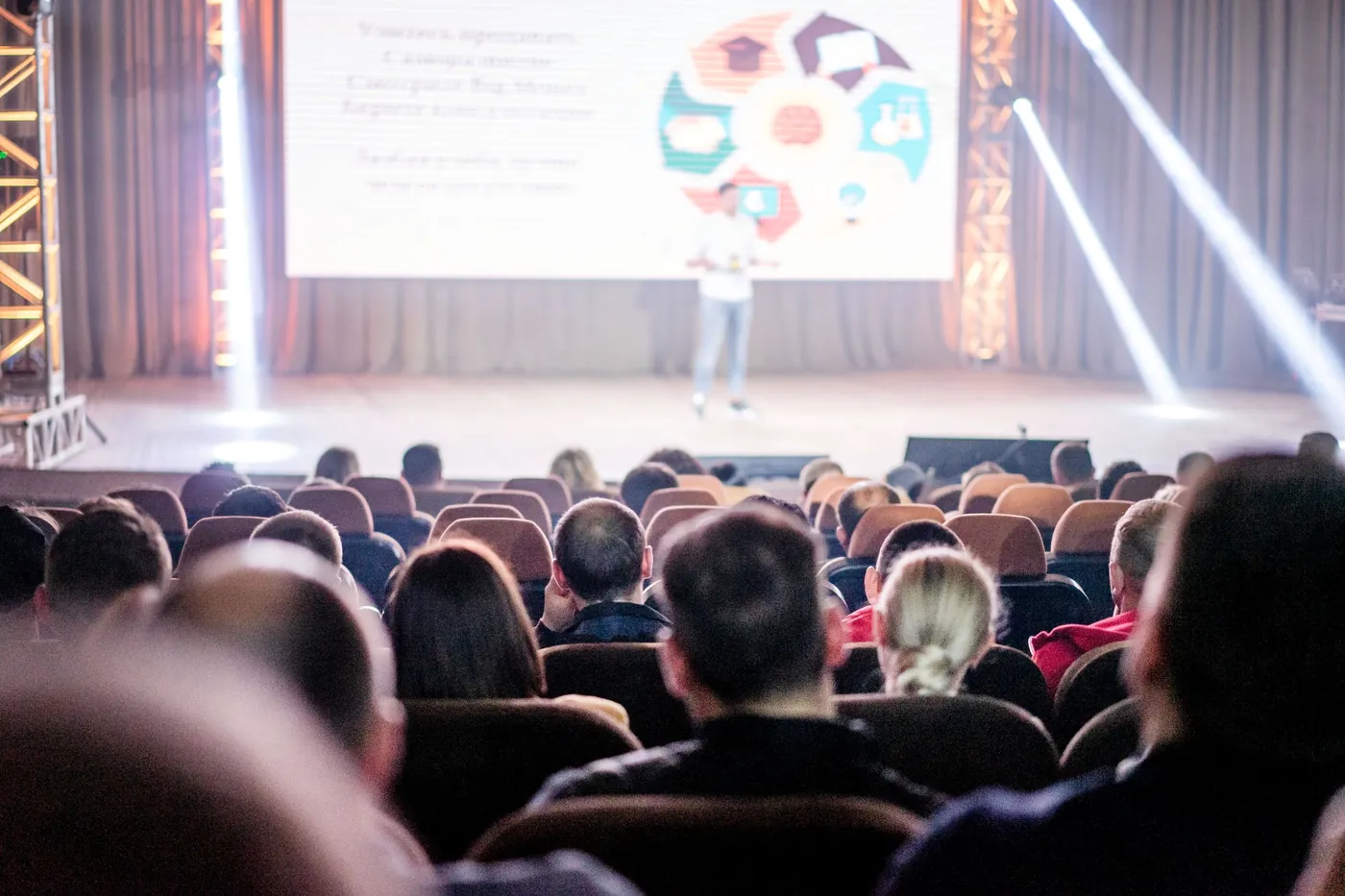 An audience seated in a hall, watching a presentation on stage.
