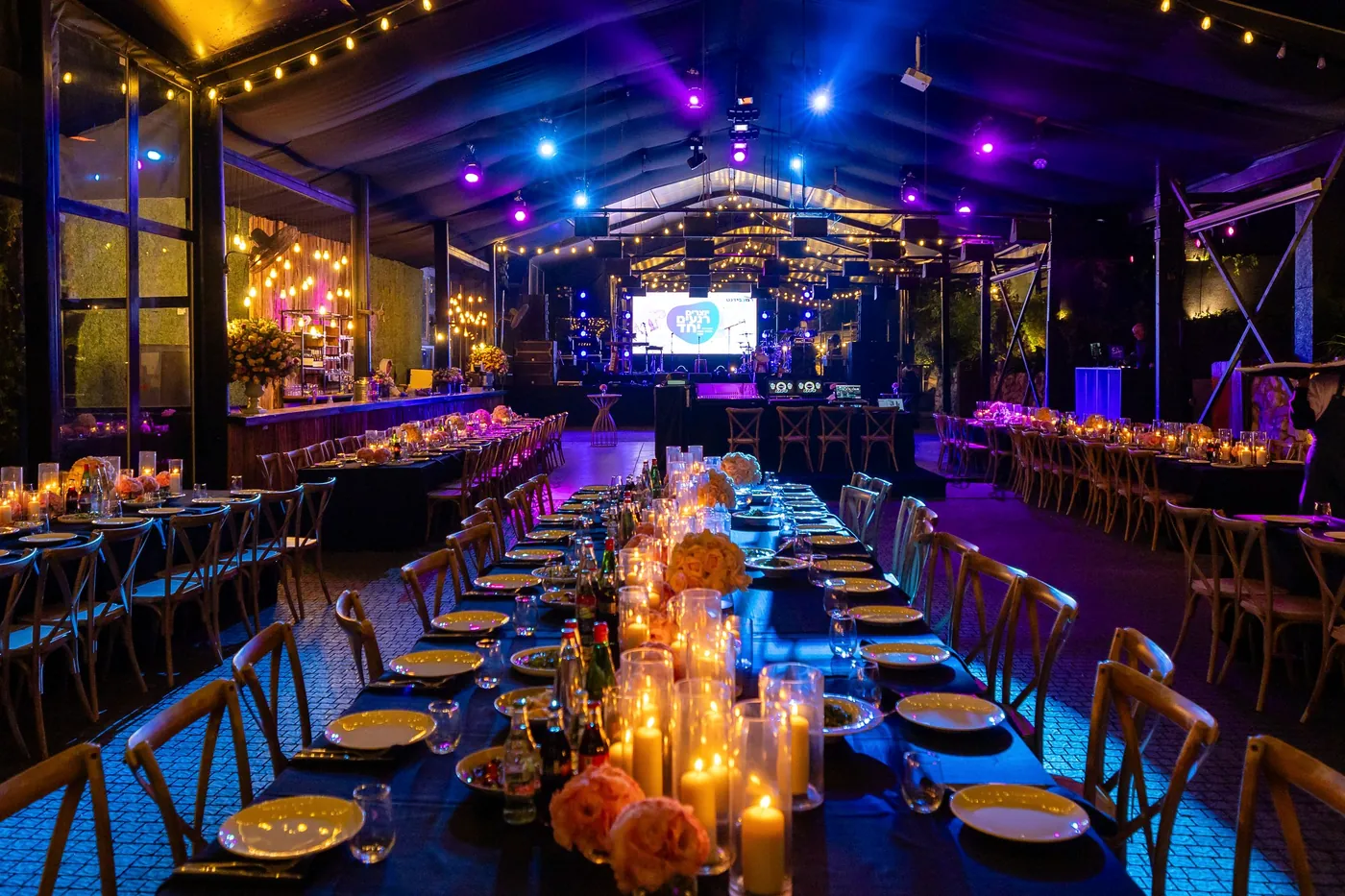 Long dinner tables set with candles and flowers for an evening event.
