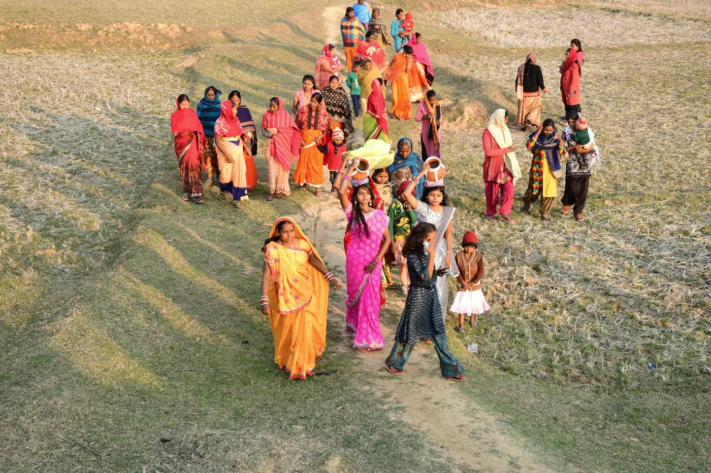 Seen from above, a line of women walk together across an open field.