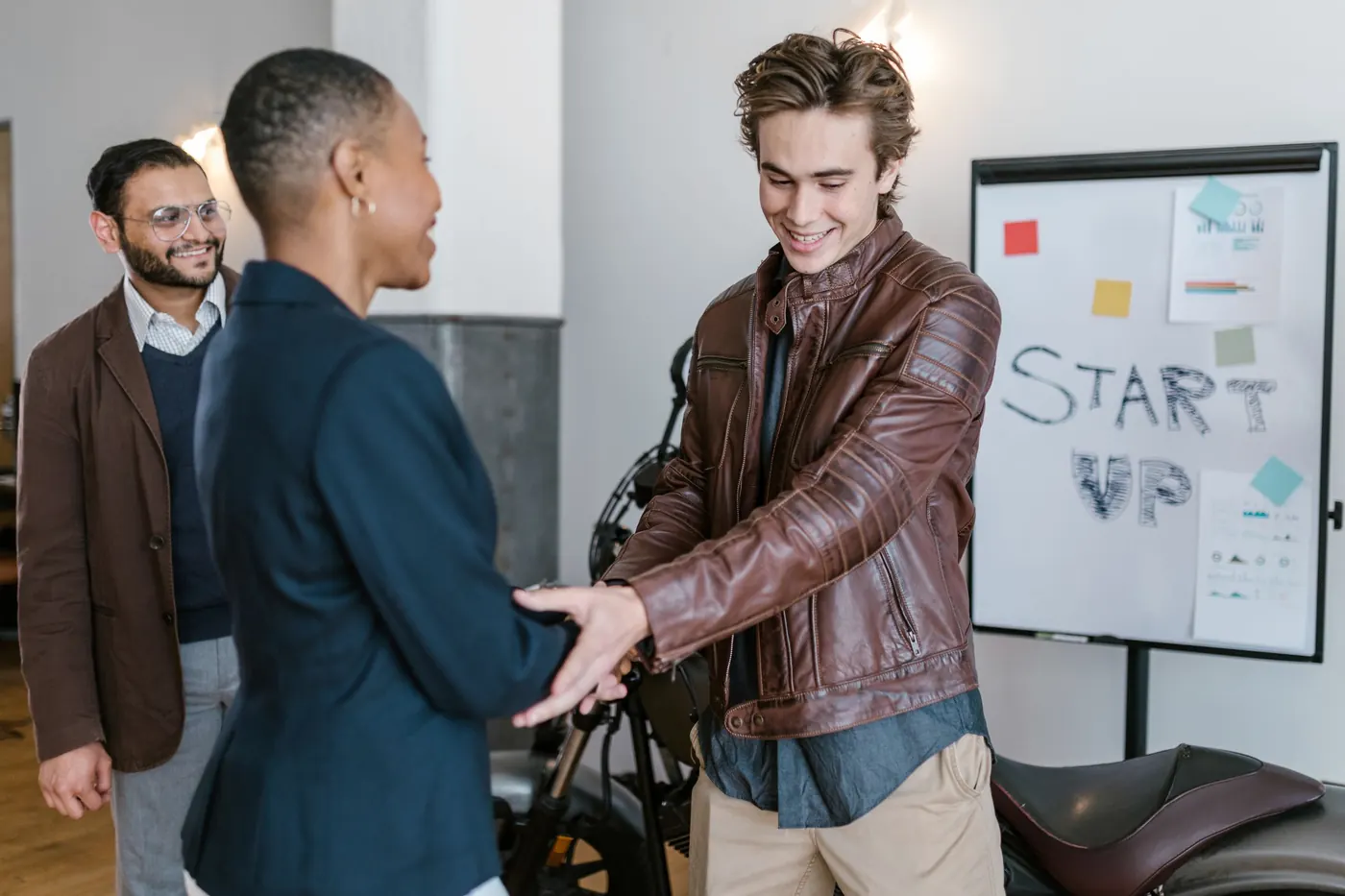 A young founder shaking hands with an investor in front of a start-up pitch board.